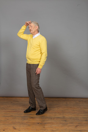 Трехчетвертный вид сбитого с толку старика, касающегося головы в желтом пуловере