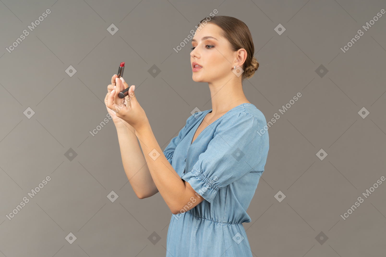 Vista de tres cuartos de una mujer joven en vestido azul abriendo lápiz labial