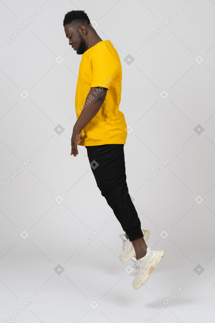 下を見下ろしている黄色のtシャツでジャンプする若い浅黒い肌の男の側面図