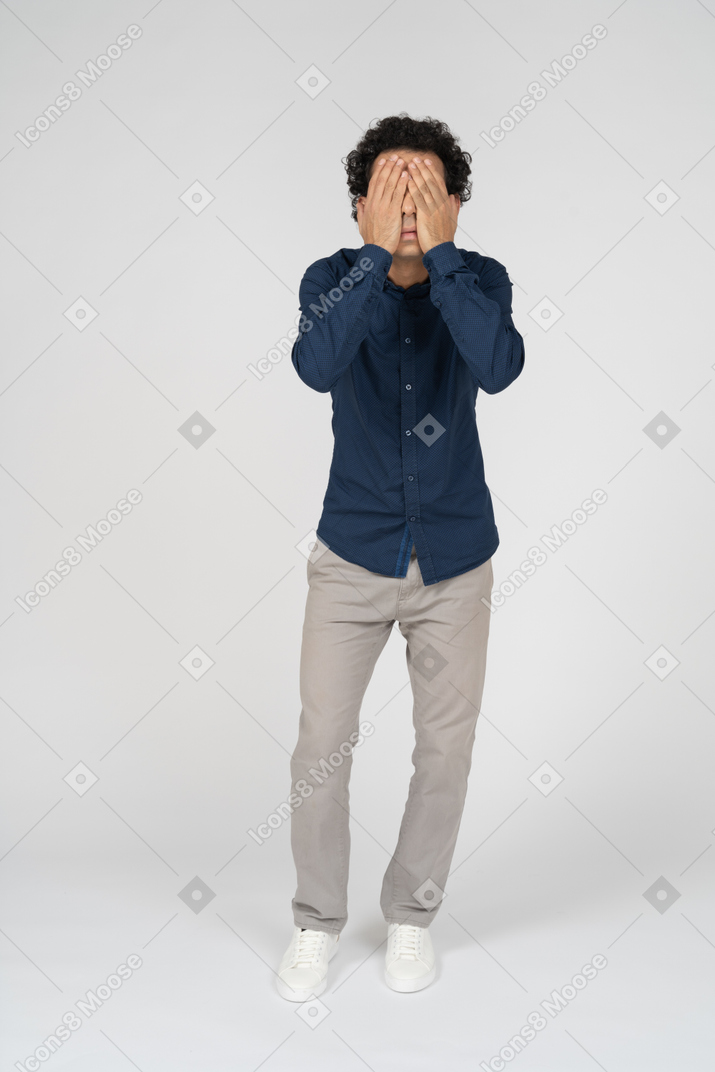 Front view of a man in casual clothes covering face with hands