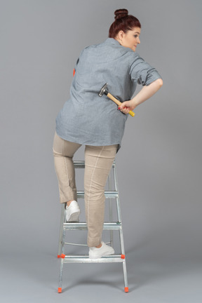 Woman  turned sideways while standing on a stepladder and holding a hammer