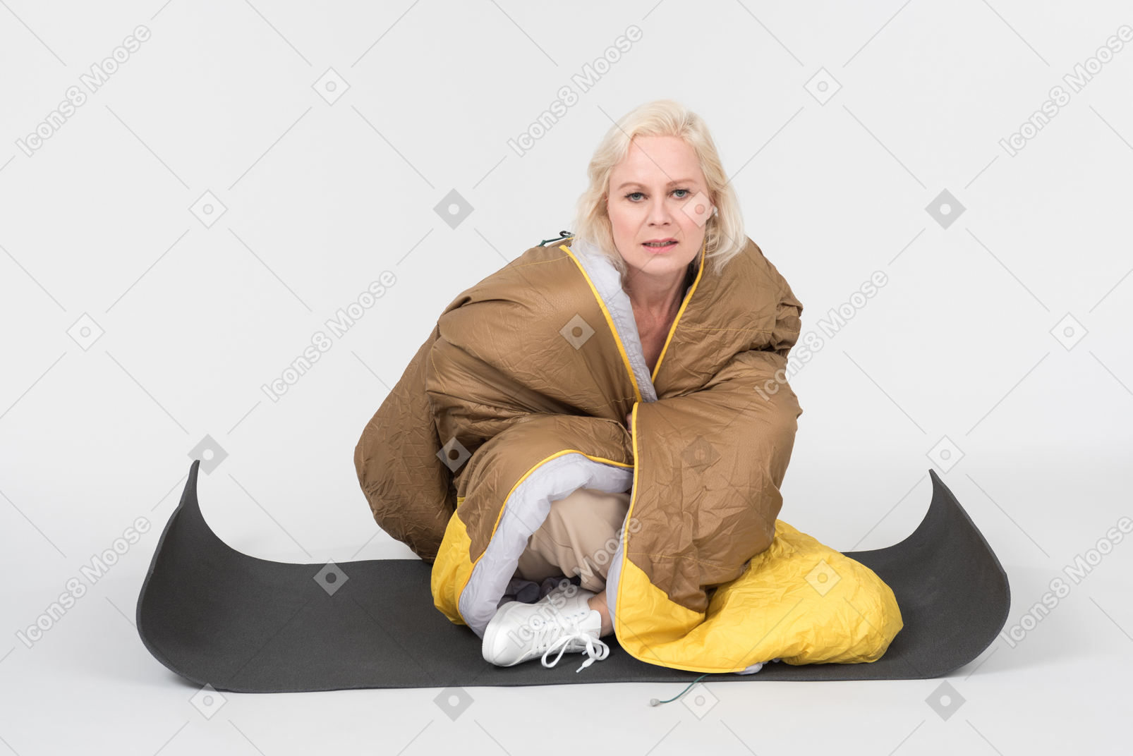 Mature woman sitting on tourist mat wrapped in blanket