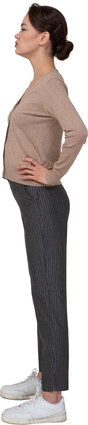 Vue latérale d'une jeune femme mécontente en pull et pantalon mettant les mains sur les hanches
