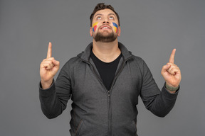 Front view of a male football fan with colorful face art raising fingers