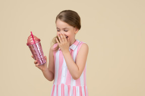Bambina carina in possesso di un bicchiere di plastica con una cannuccia