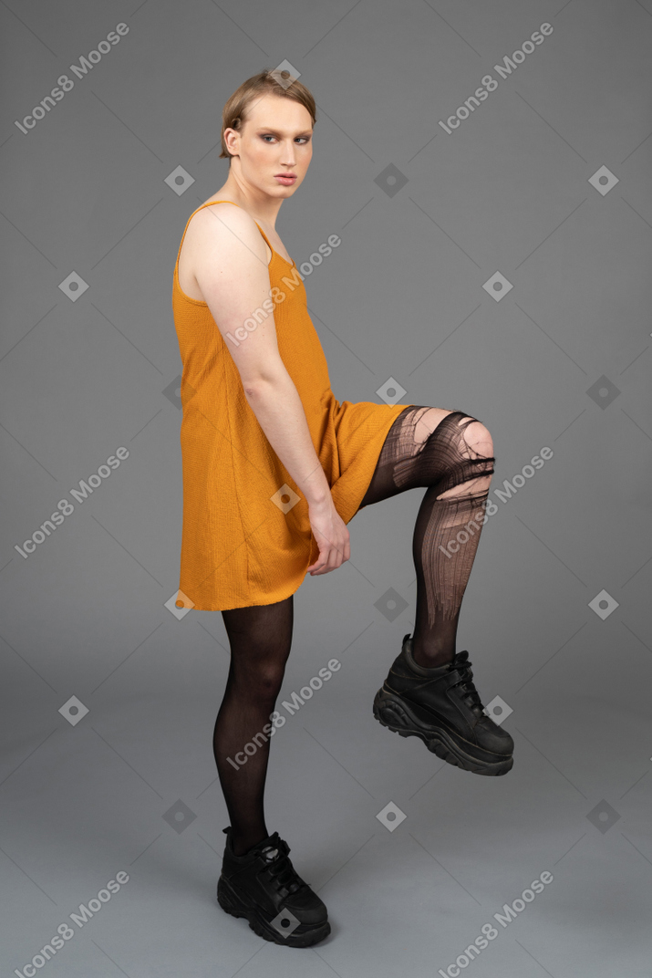 Retrato de uma pessoa genderqueer em vestido laranja levantando o joelho