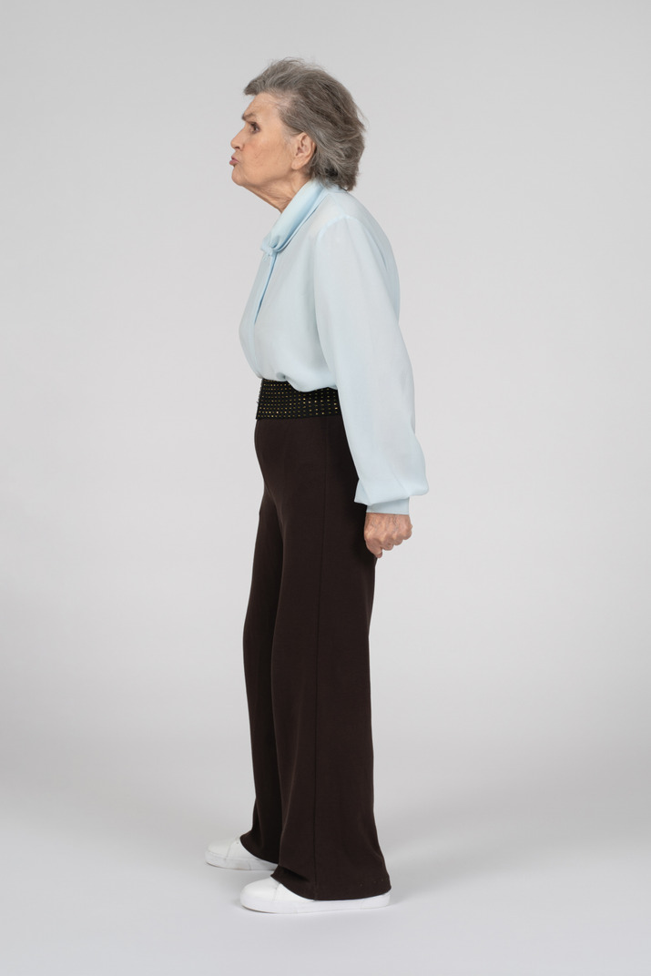 Back view of an old woman in blouse and trousers putting hand on hip