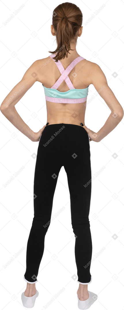 Vista posterior de una jovencita en ropa deportiva poniendo las manos en las caderas