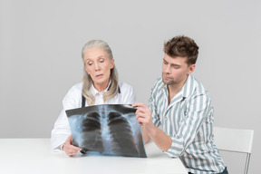 Une femme médecin âgée et un patient qui regardent ensemble une photographie aux rayons x