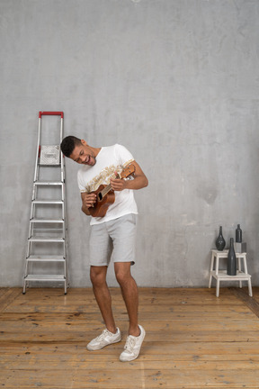 Visão de três quartos de um homem inclinado para o lado e tocando ukulele alegremente