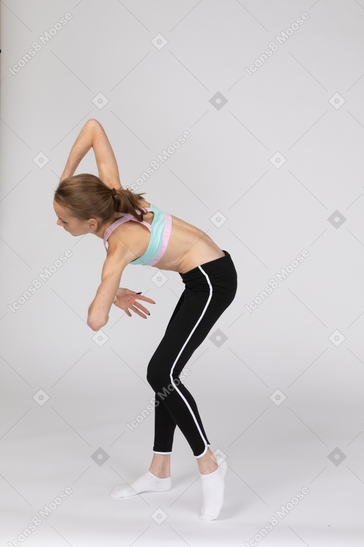 Vista lateral de una jovencita en ropa deportiva inclinándose hacia adelante y gesticulando