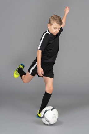 Three-quarter view of a kid boy in football uniform kicking a ball