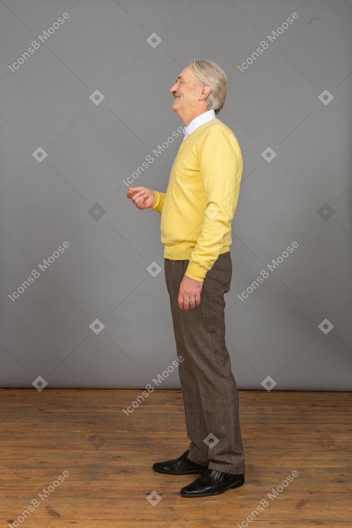 Vue latérale d'un vieil homme gesticulant portant un pull jaune et regardant de côté en souriant