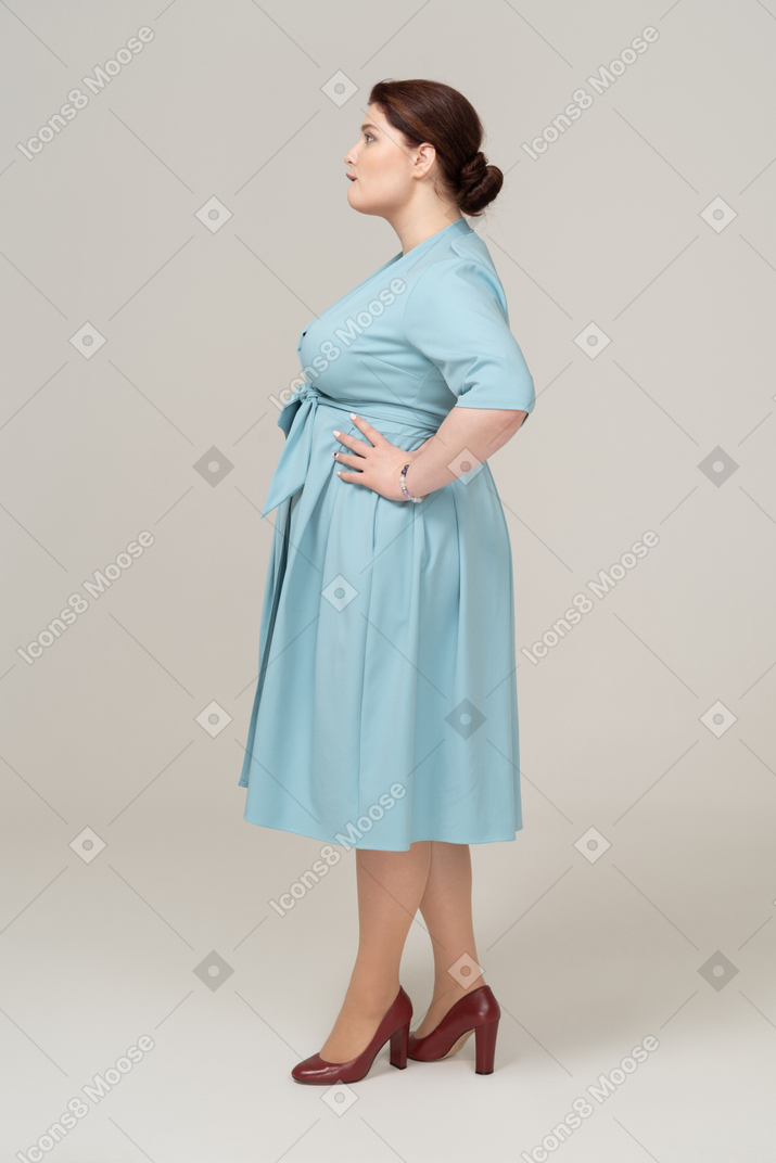 Vista laterale di una donna in abito blu in posa con le mani sui fianchi