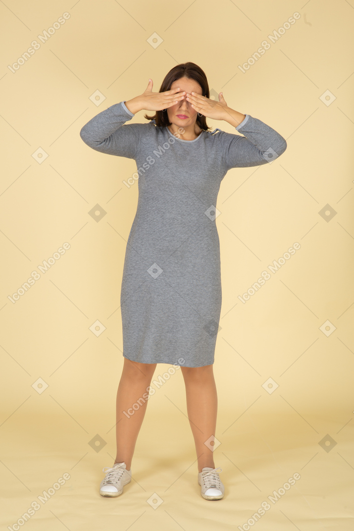 Front view of a woman in grey dress closing her eyes with hands