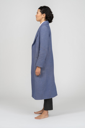 Angry looking young woman in long blue coat standing in profile