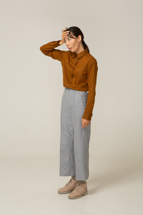 Three-quarter view of a tired young asian female in breeches and blouse touching head