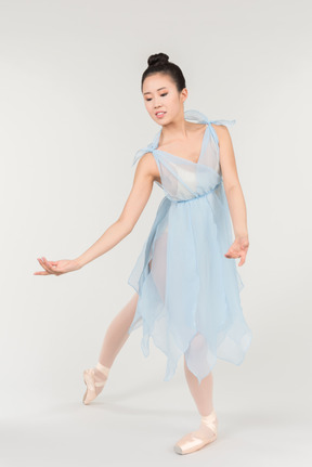 Junge asiatische ballerina in einem transparenten hellblauen kleid, das in einer klassischen balletthaltung steht