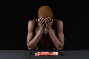 Vista frontal de um jovem homem afro retraído sentado perto de uma carne