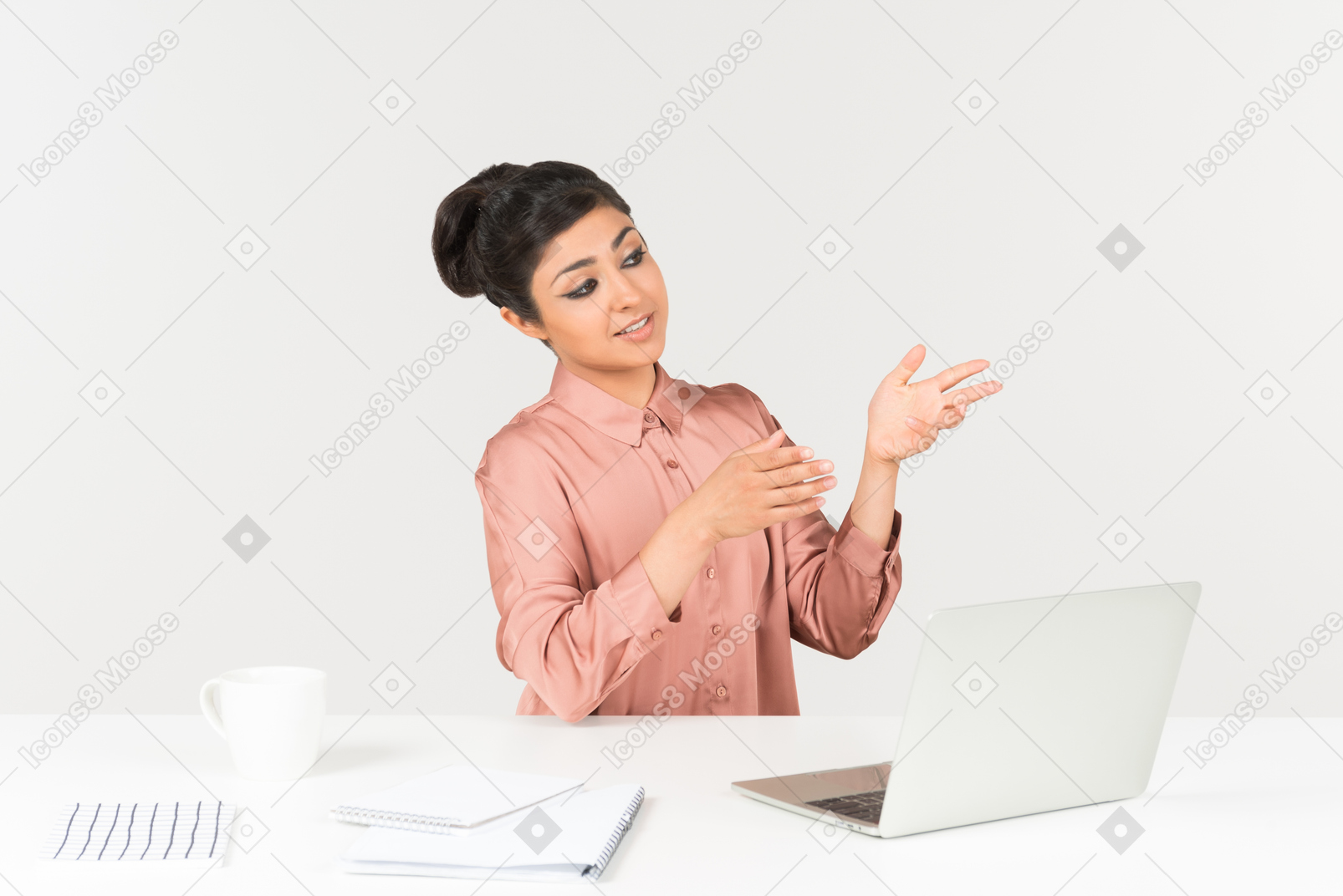 Молодая индийская женщина сидит за офисным столом и указывая рукой