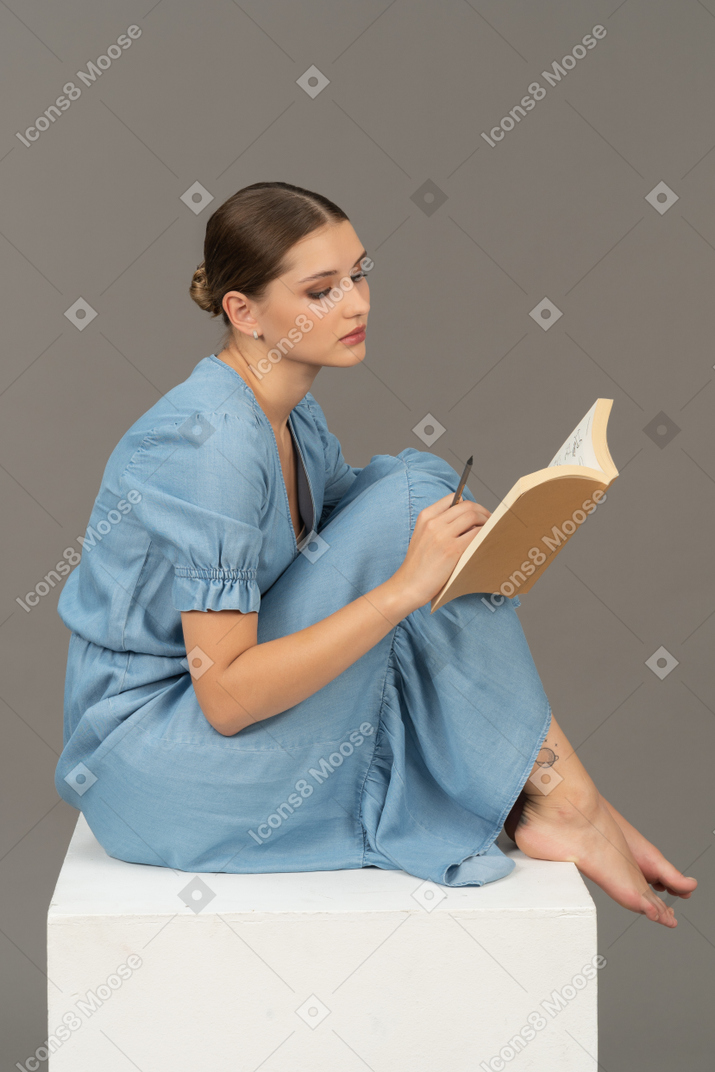 年轻女子坐在立方体上并在笔记本上写字的侧视图