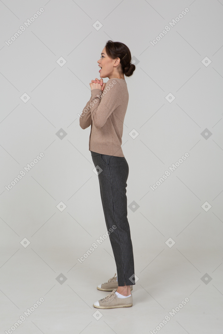 Side view of a delighted young lady in beige pullover holding hands together