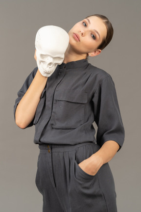 Front view of a young woman in a jumpsuit holding a plaster skull