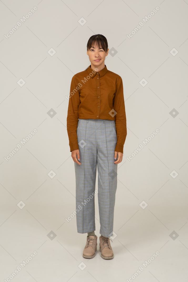 Front view of a winking young asian female in breeches and blouse standing still