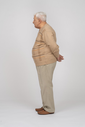 一位身穿休闲服、双手背在身后站立的老人的侧视图
