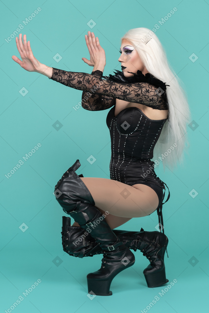 Drag queen squatting in high boots with arms stretched forward