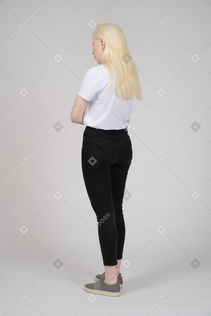 Three-quarter back view of a young blonde woman standing with arms crossed