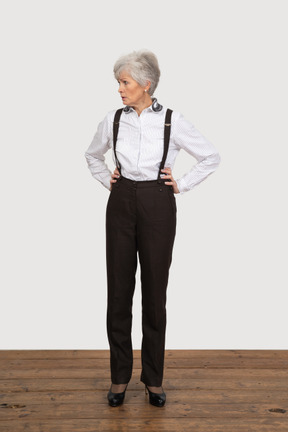 一个不高兴的老太太，把手放在臀部上的办公服装的前视图