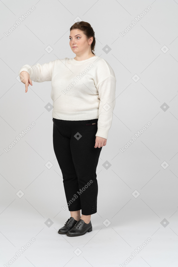 Donna grassoccia in maglione bianco che punta verso il basso con un dito