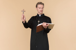 Catholic priest holding cross and reading a bible