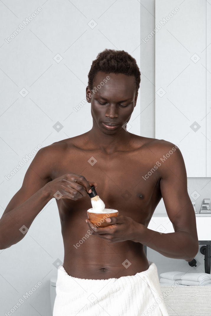 A man in a towel mixing shaving cream in a bowl