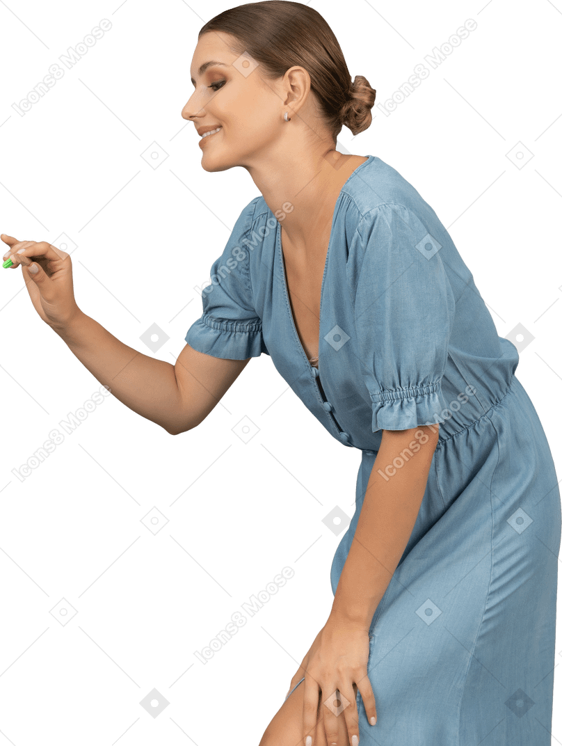 Vista laterale di una giovane donna in abito blu che tiene in mano uno spazzolino da denti e si sporge in avanti