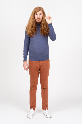 Front view of a young man in casual clothes pointing up with a finger