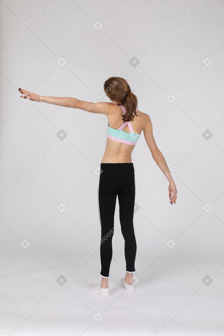 Three-quarter back view of a teen girl in sportswear outstretching her hand and tilting head