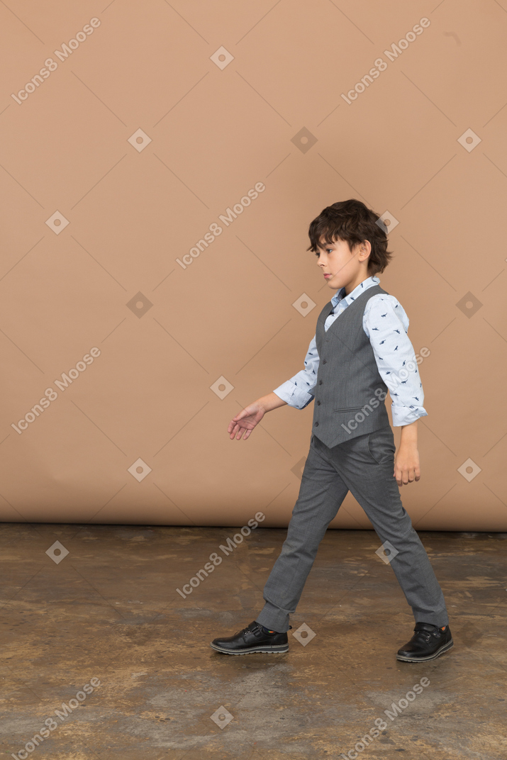 一个穿着西装的可爱男孩走路的侧视图