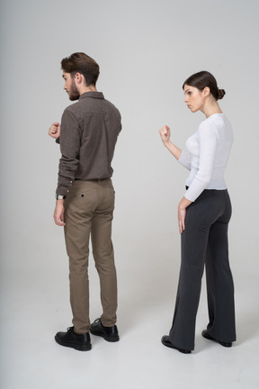 Three-quarter back view of a strict young couple in office clothing showing fist