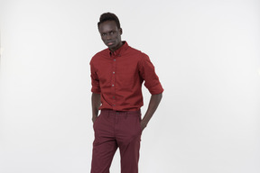 A young black man in a red shirt with rolled up sleeves and dark red pants standing alone on the white background