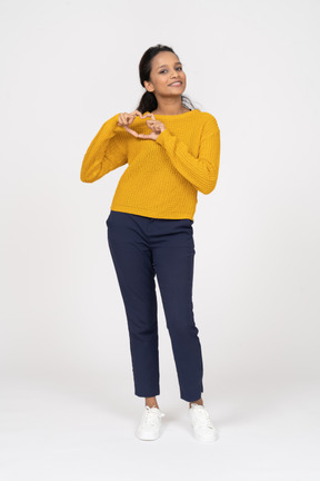 Front view of a happy girl in casual clothes showing heart sign and looking at camera