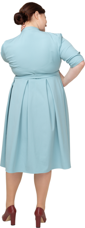 Вид сзади женщины в синем платье позирует с рукой на бедре