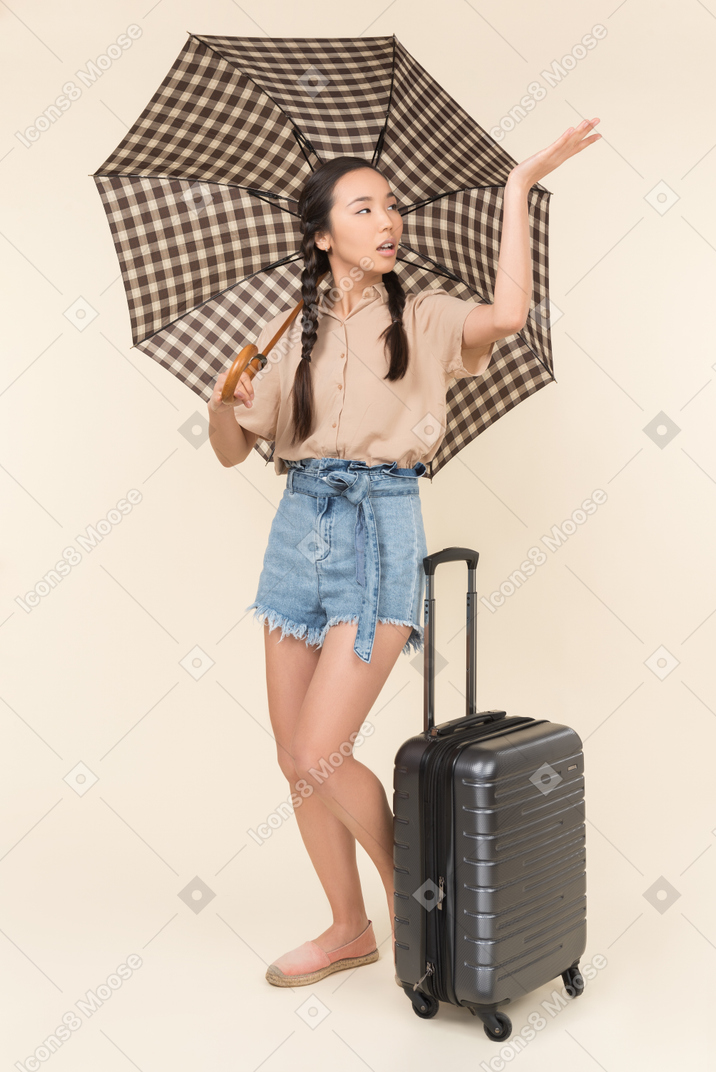 Young woman with suitcase and umbrella checking for rain