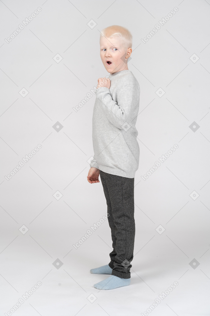 Little boy standing scared and looking behind back