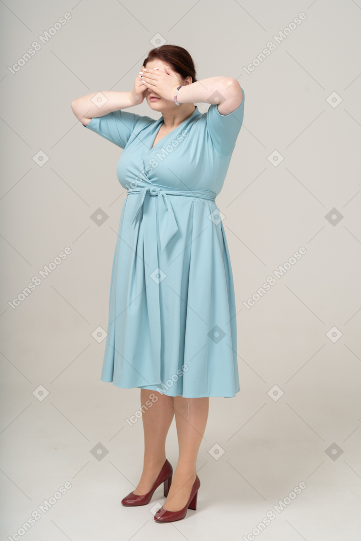 Vista lateral de uma mulher de vestido azul fechando os olhos com as mãos