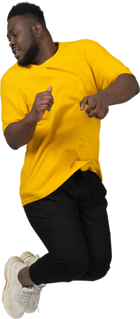 Front view of a jumping young dark-skinned man in yellow t-shirt