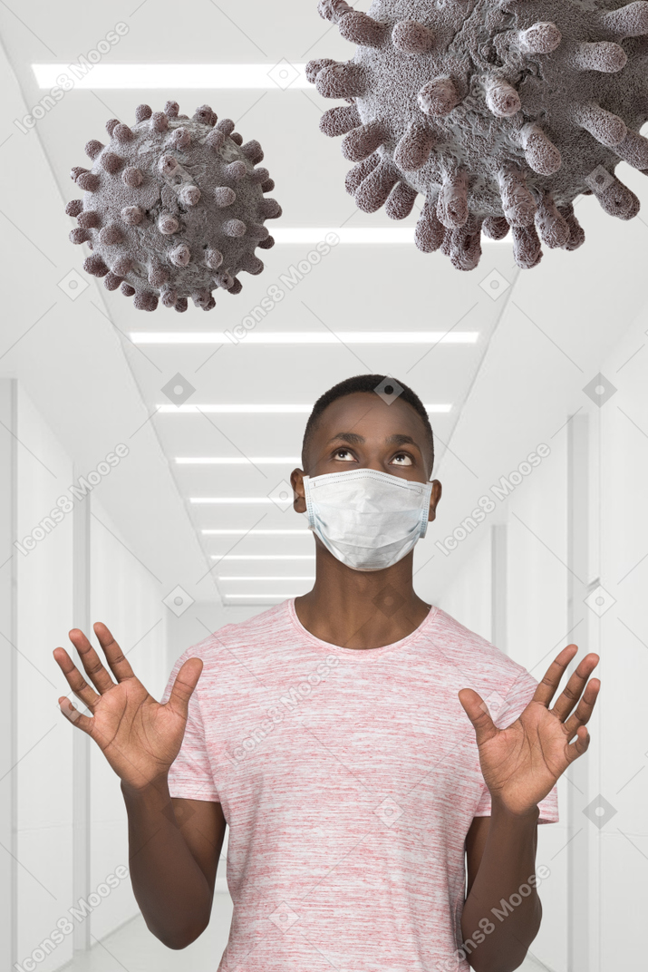 A man wearing a face mask standing in a hallway with coronavirus floating in the air