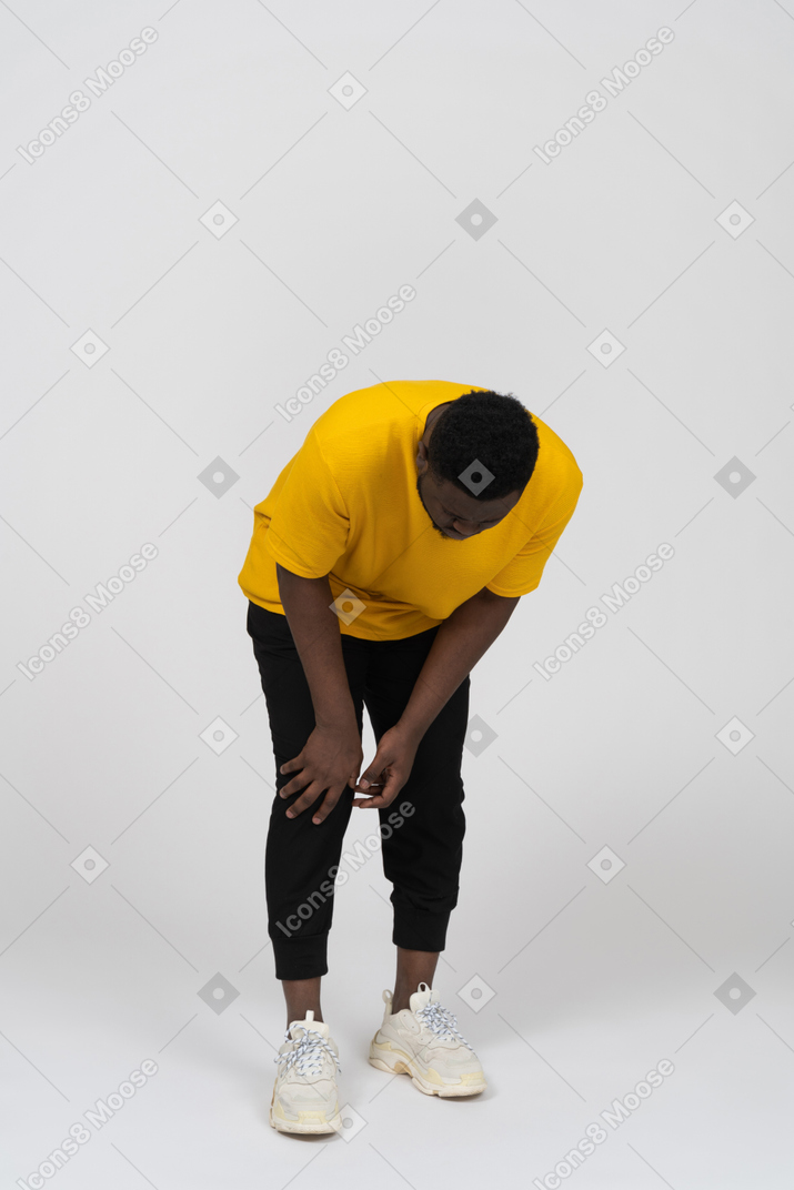 一个身穿黄色 t 恤、摸着膝盖的深色皮肤男子的前视图