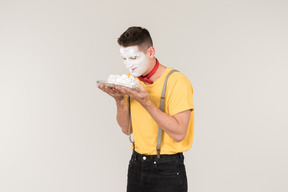 Male clown with cake cream on his face holding a cake